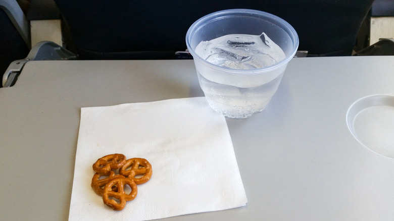 plastic cup of clear liquid and four small pretzels on an airplane tray