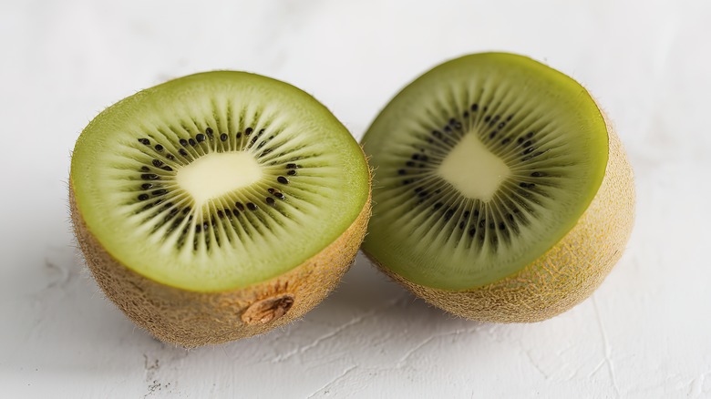 person slicing green kiwi with sharp knife over wooden cutting board