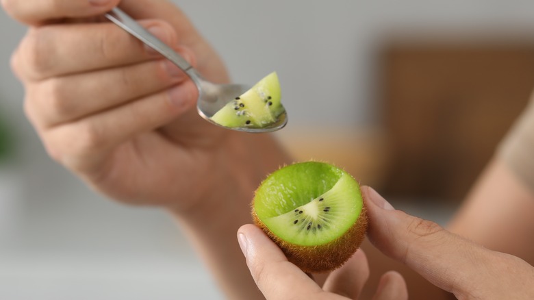 person scooping green kiwi flesh from skin with a spoon