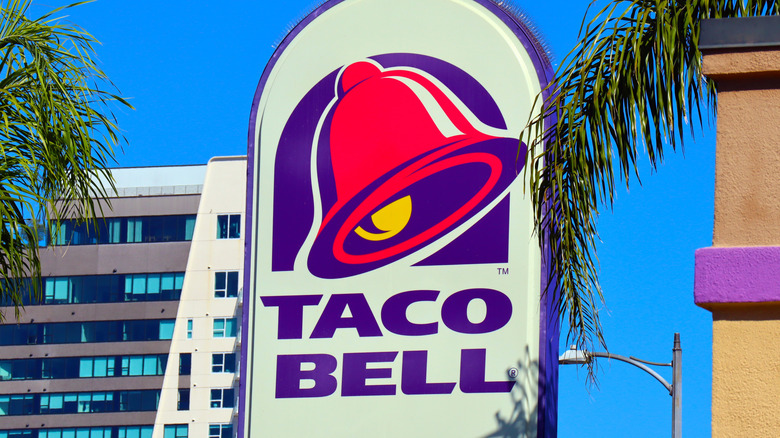 A sign for a Taco Bell location, thronged by palm trees.