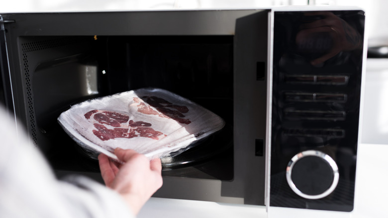 hand putting frozen meat into microwave