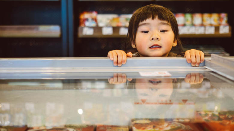 a child peers into the freezer section at the grocery store