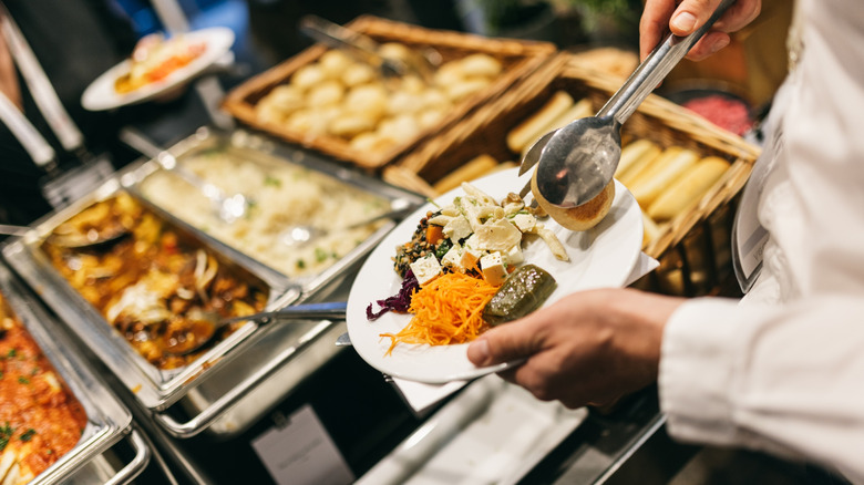 person filling their plate with various foods at a buffet