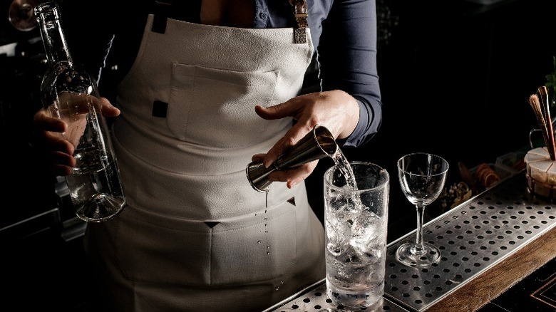 A bartender expertly pours vodka into a glass behind the bar.