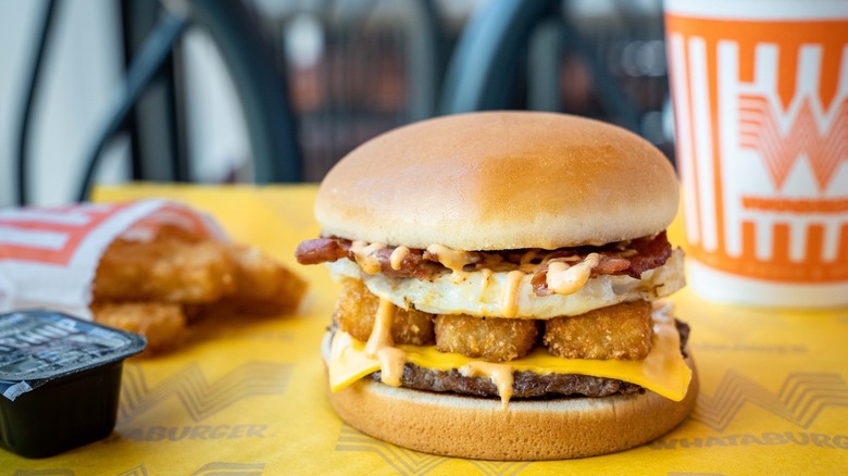 A Whataburger Breakfast Burger next to ketchup, hashbrowns and a cup