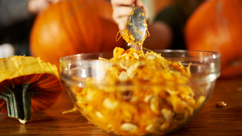 Pumpkin guts in a bowl and sticking to a spoon