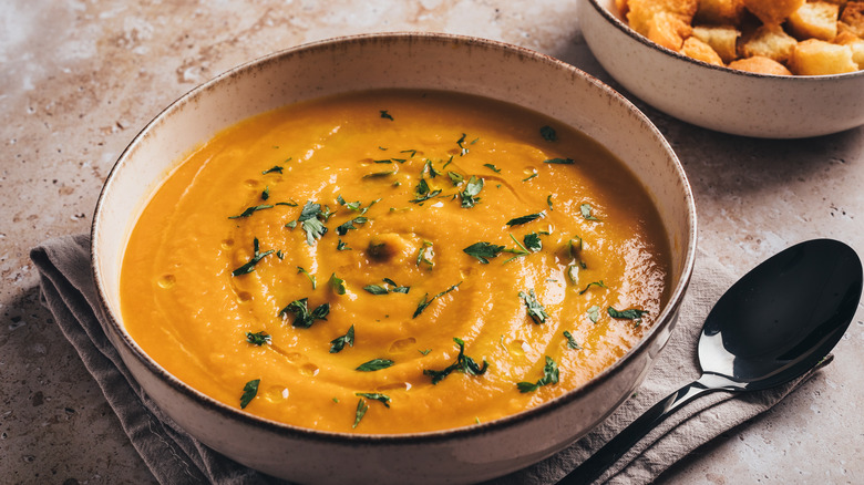 A bowl of pumpkin soup beside a spoon