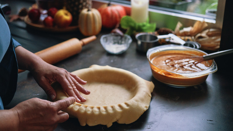 woman forming pie crust for pumpkin pie with bowl of filling nearby