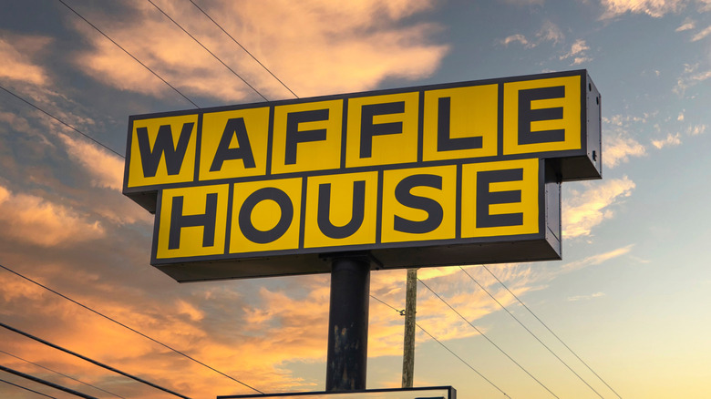 A Waffle House sign with a telephone pole behind it at dusk.