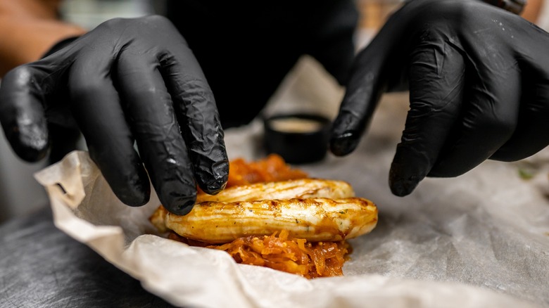 gloved hands preparing a grilled chicken sandwich