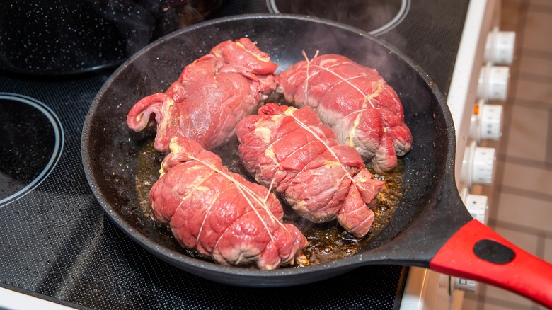 Four beef olives being cooked in a frying pan