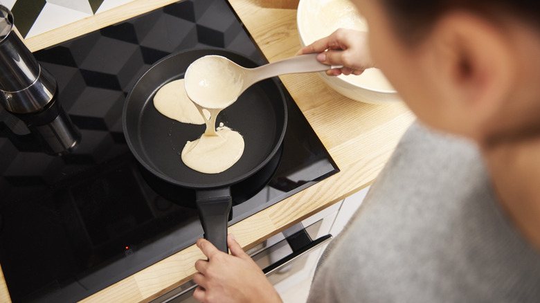 Man making pancakes in a black pan.