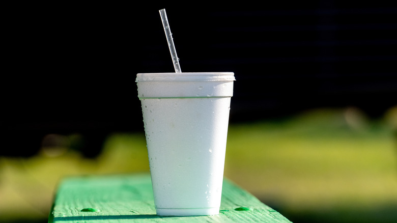 A styrofoam cup and plastic straw sit on a bench