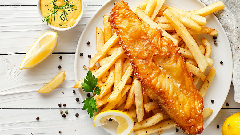 Plate of fried fish with fries, lemons, and peppercorns