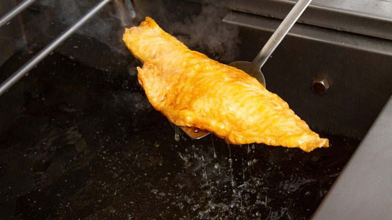 Removing golden, crispy fried fish from hot oil with a spatula