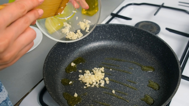 A person adding chopped garlic to a black frying pan.