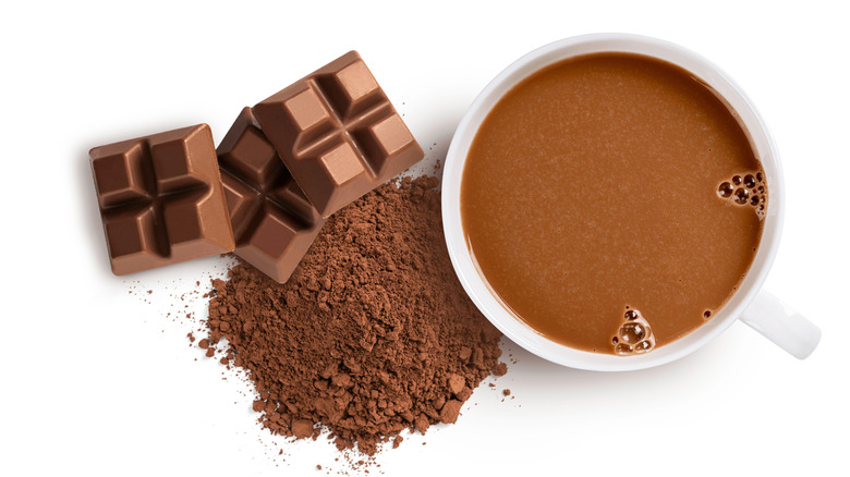 Cup of chocolate drink next to cocoa powder and chocolate bars