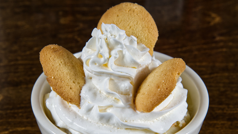 vanilla wafers and whipped cream on top of bananas in a small, white cup