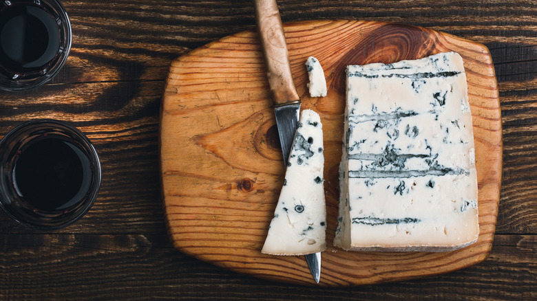 Wedge of cut blue cheese with knife on wood board