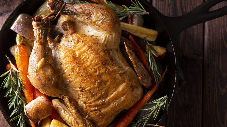 Whole, crispy roast chicken in a cast iron skillet with roasted veggies