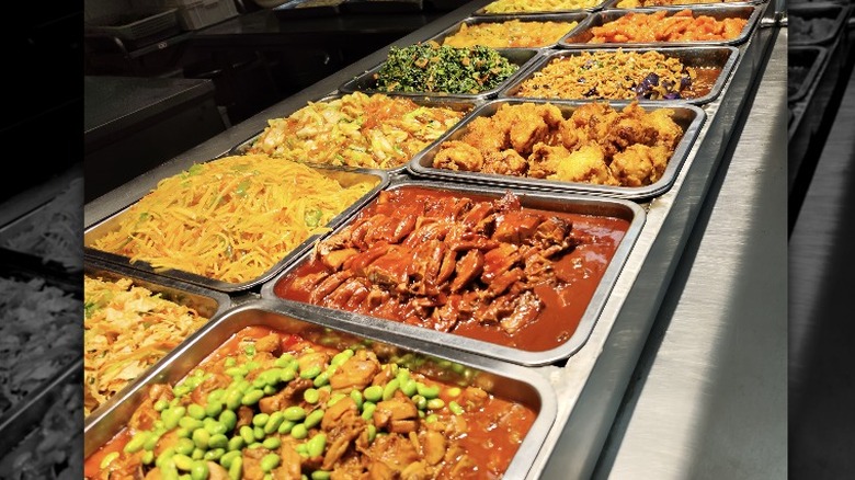 Buffet style gathering with many options on a large table and people on either side adding food to their plates.