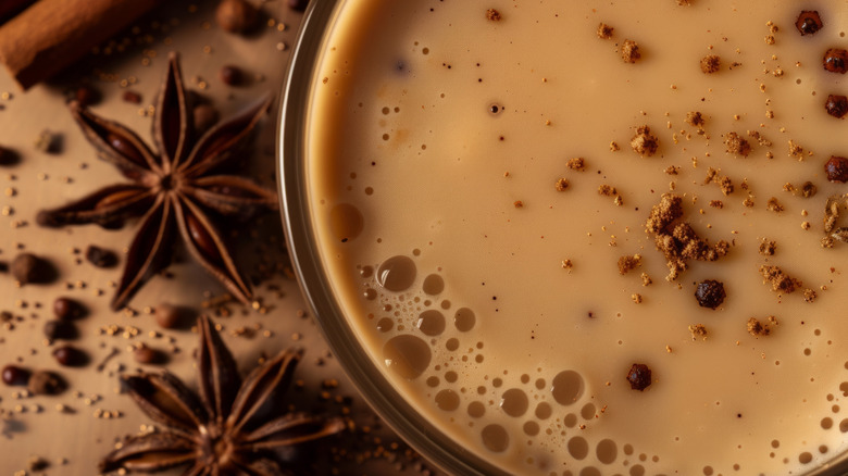 A close up of a chai latte topped with cinnamon surrounded by spices and cloves