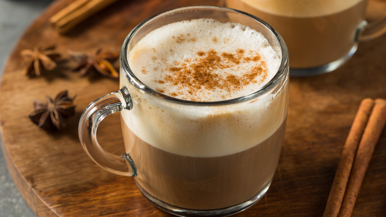 A glass mug of chai latte with foam topped with cinnamon