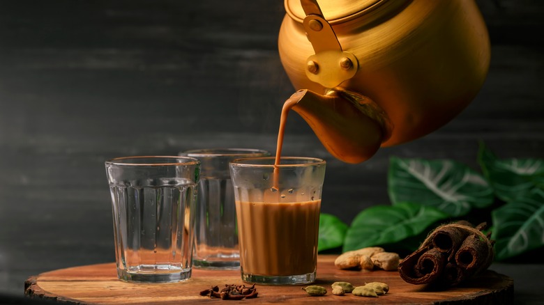 A tea kettle pours out Indian masala chai into glass cups