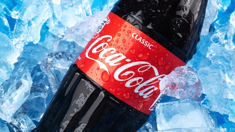 A bottle of Coca-Cola resting in ice.