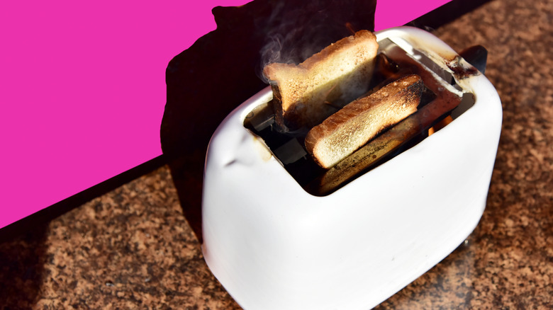 Smoke rises from burnt toast inside a toaster