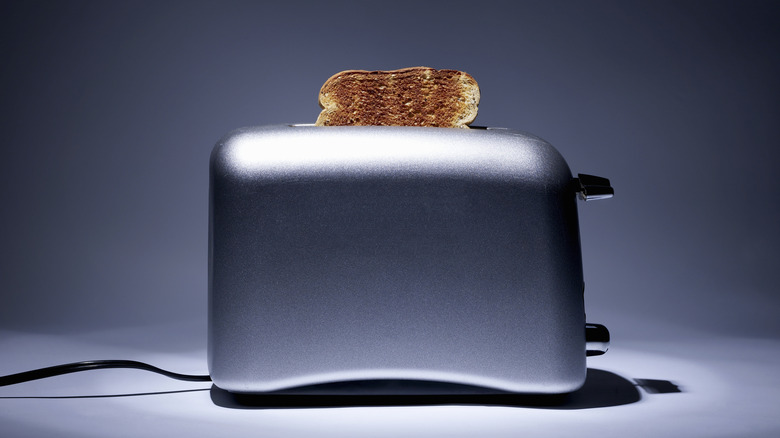 A silver toaster with a single piece of toast