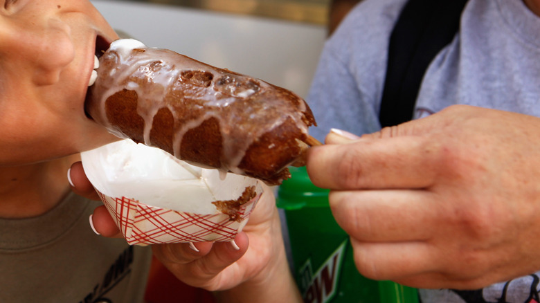 a woman holds a deep fried butter on a stick for her son to bite