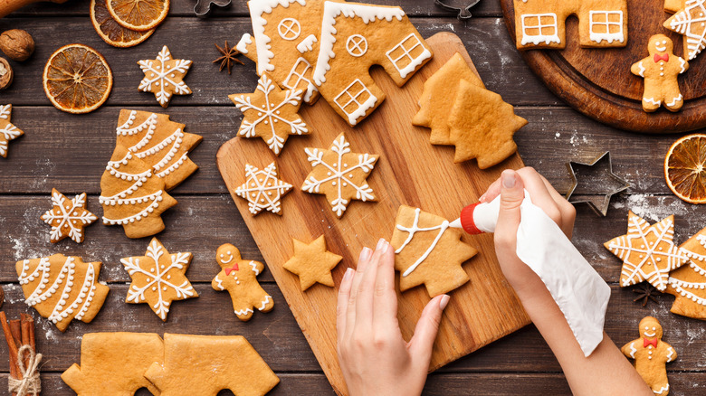 Hands decorating gingerbread cookies with white royal icing