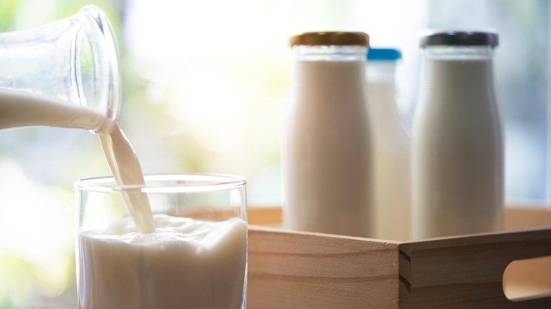 Milk jugs in a wooden crate and a cup getting filled with milk as well.