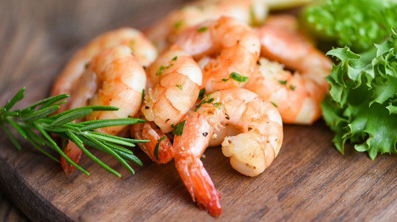 Cooked shrimp on a wooden board with fresh herbs