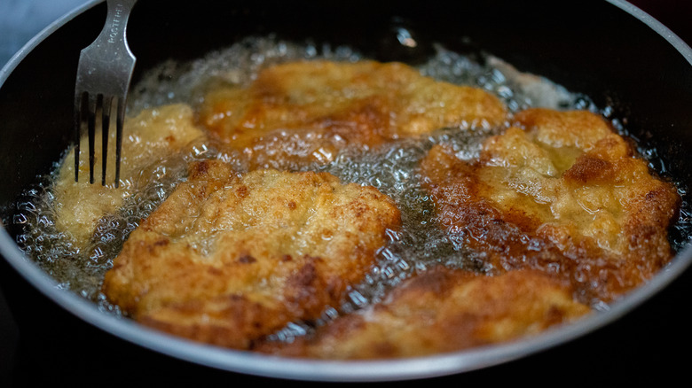 A person frying chicken in oil while testing it with a fork