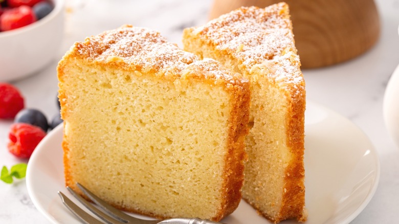 Two slices of vanilla pound cake dusted with sugar on a round white plate