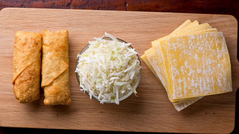 Two fried egg rolls next to shredded cabbage and dough wrappers