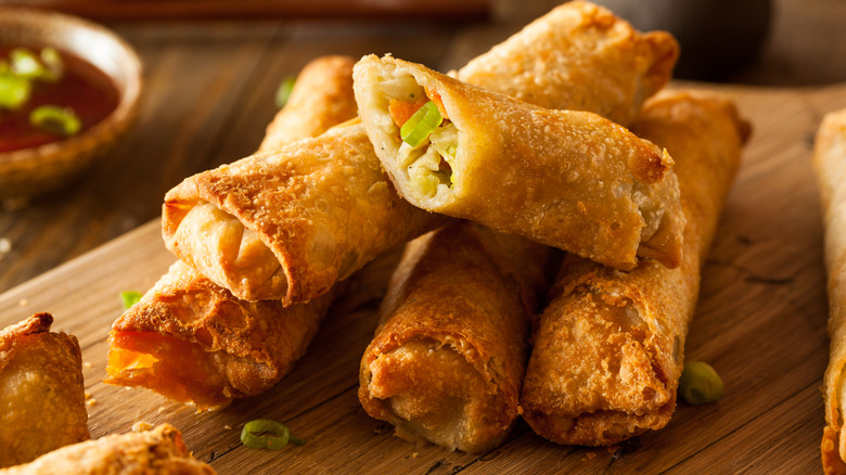 A stack of crispy homemade egg rolls on a wooden cutting board