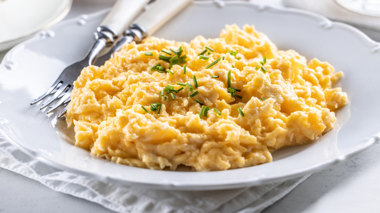 Scrambled eggs on an elegant white plate with chives next to silverware