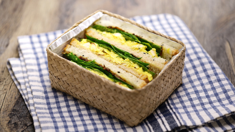 sliced chicken salad sandwiches in a small box on a tea towel