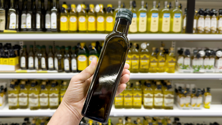 Someone holding a bottle of olive oil in front of an olive oil aisle