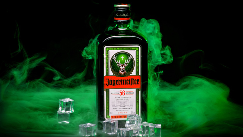 Jägermeister on a black background with green smoke and ice cubes.