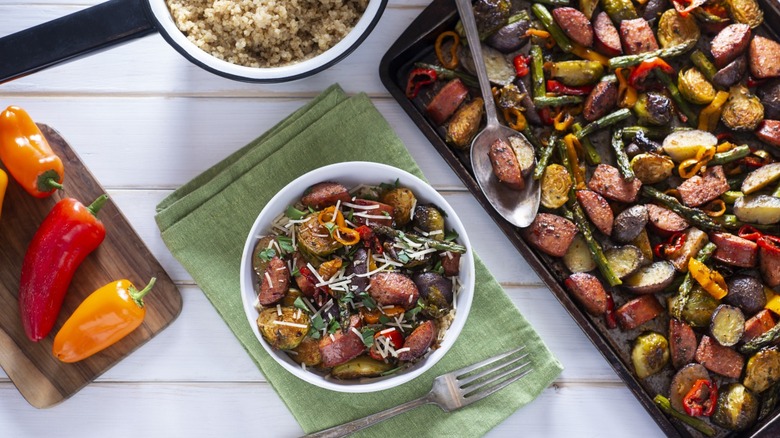 Sheet pan and bowl with roasted veggies near rice and bell peppers