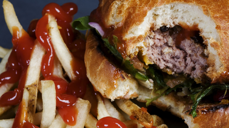 A half-eaten burger is shown with French fries