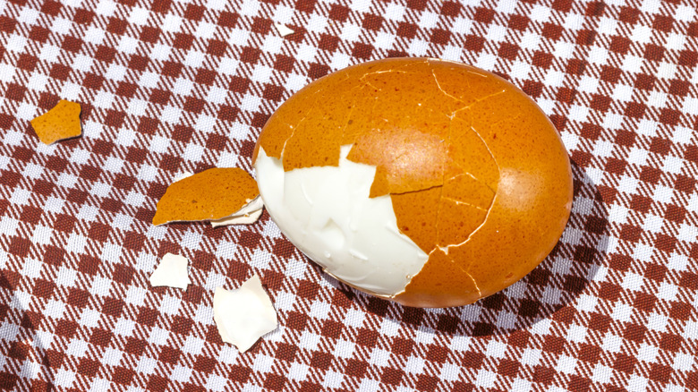 A partially peeled hard-boiled egg rests on picnic cloth