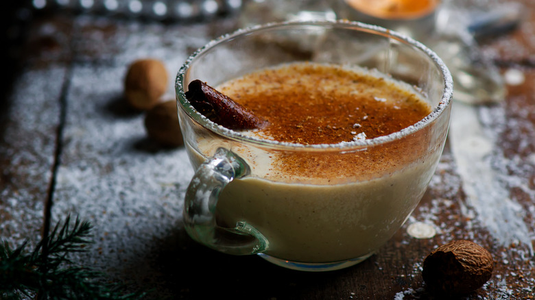 A cup of eggnog topped with cinnamon and a cinnamon stick on a rustic background