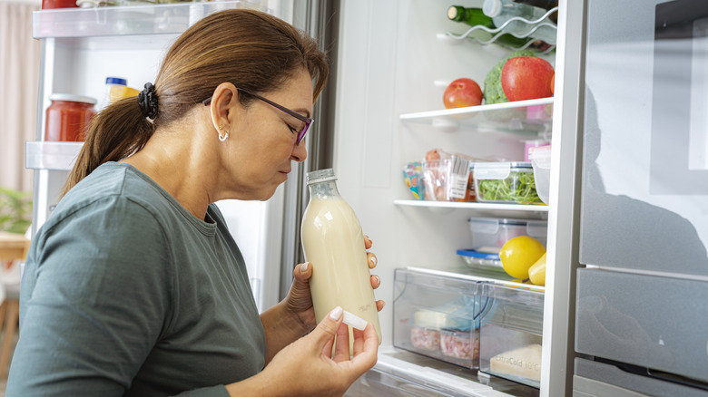 A woman grabbing a full beverage from her fridge and smelling it