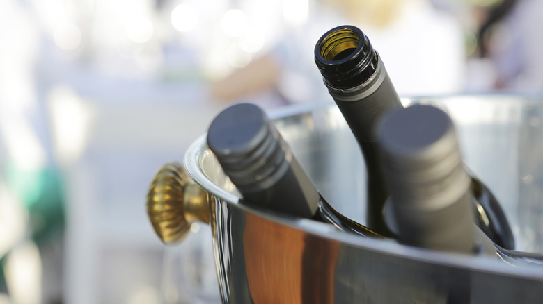 three bottles of wine in a bucket, two closed and one opened