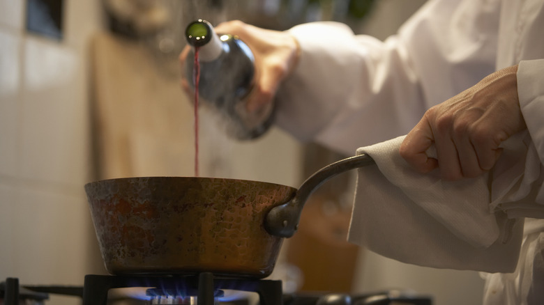 person pouring red wine into saucepan on stove